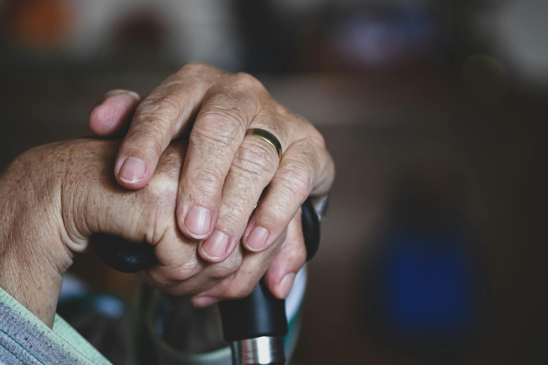 Elderly hands clasped gently over a cane handle