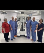 A large white robot with six people stood around it, they are in a hospital with scrubs on.