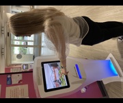 A woman with her left arm outstretched, using a touch screen sign-in kiosk