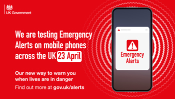A phone showing a warning. Text to the left reads "We are testing Emergency Alerts on mobile phones across the UK 23 April. On our way to warn you when lives are in danger"