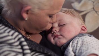 A woman gently kisses a sleeping baby on the head, conveying warmth and tenderness. The baby rests peacefully in her arms, with soft lighting and a cosy atmosphere.